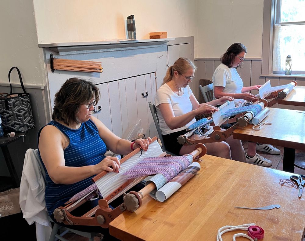 Three women weaving scarves on rigid heddle looms.