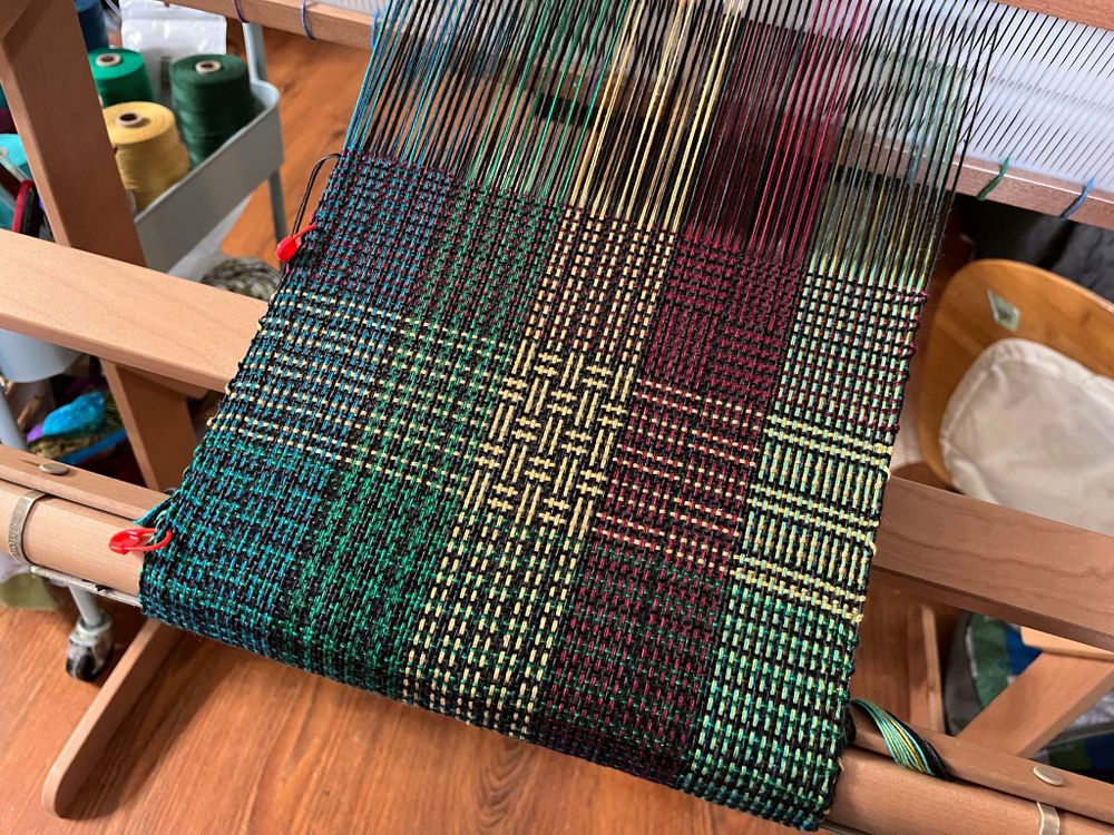 A multi-coloured cotton scarf on a rigid heddle loom with squares of many different patterns.