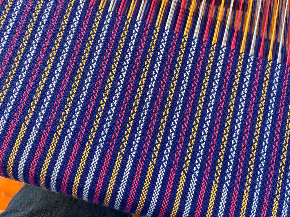 A blue, pink, and gold striped tea towel on a counter-balance floor loom.