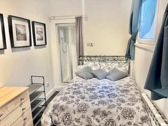 bedroom with a twin bed and an unusually placed shower. the shower doors are almost immediately to the left of the head of the bed.