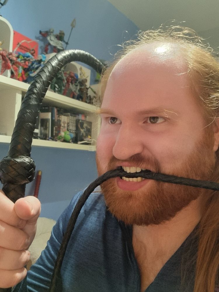 A horrific goblin man holds a whip by the handle with the other end in his awful teeth