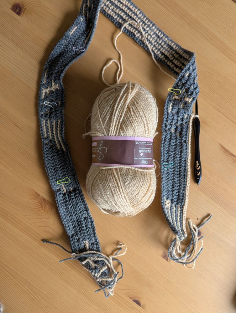 Dark Grey and sand coloured piece of crochet on wooden surface with black crochet hook 