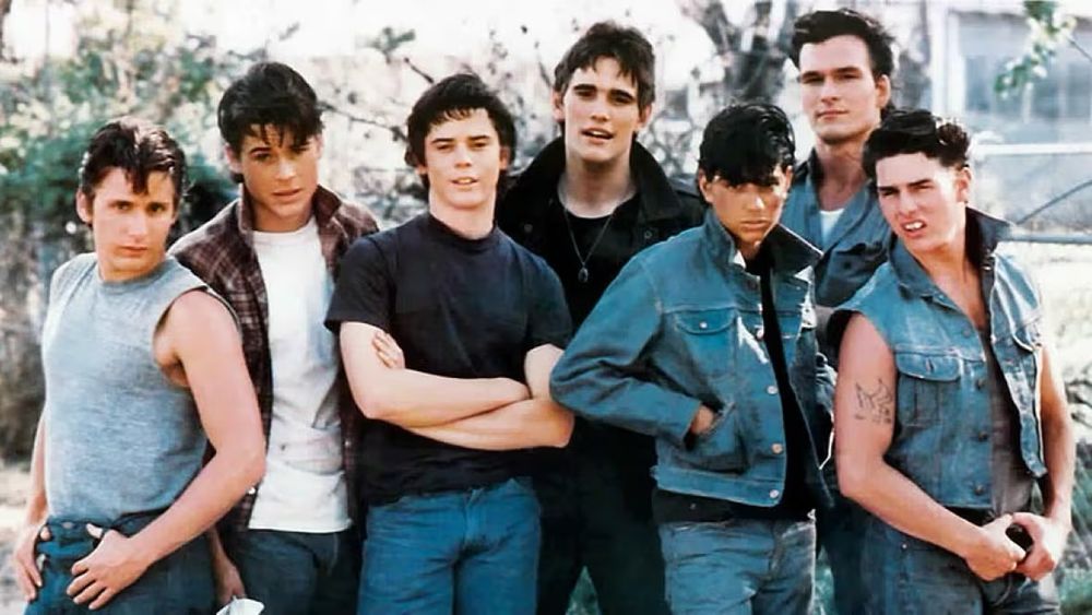 Set photo from the 1983 film version of SE Hinton's novel The Outsiders, about the clash between rich kids and poor kids in Tulsa, Oklahoma in the early 1960s. From left to right, in period bluejeans, T-shirts, and denim jackets,: Emilio Estevez, Rob Lowe, C. Thomas Howell, Matt Dillon, Ralph Macchio, Patrick Swayze, Tom Cruise.