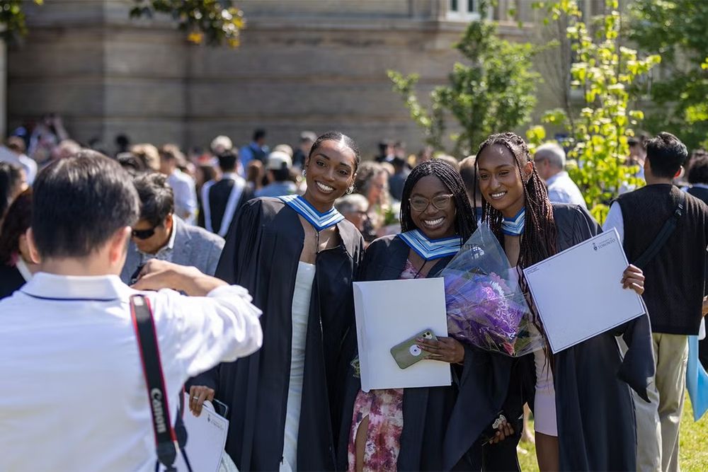Three new U of T graduates smile for the cameras outside Convocation Hall on the St. George campus 