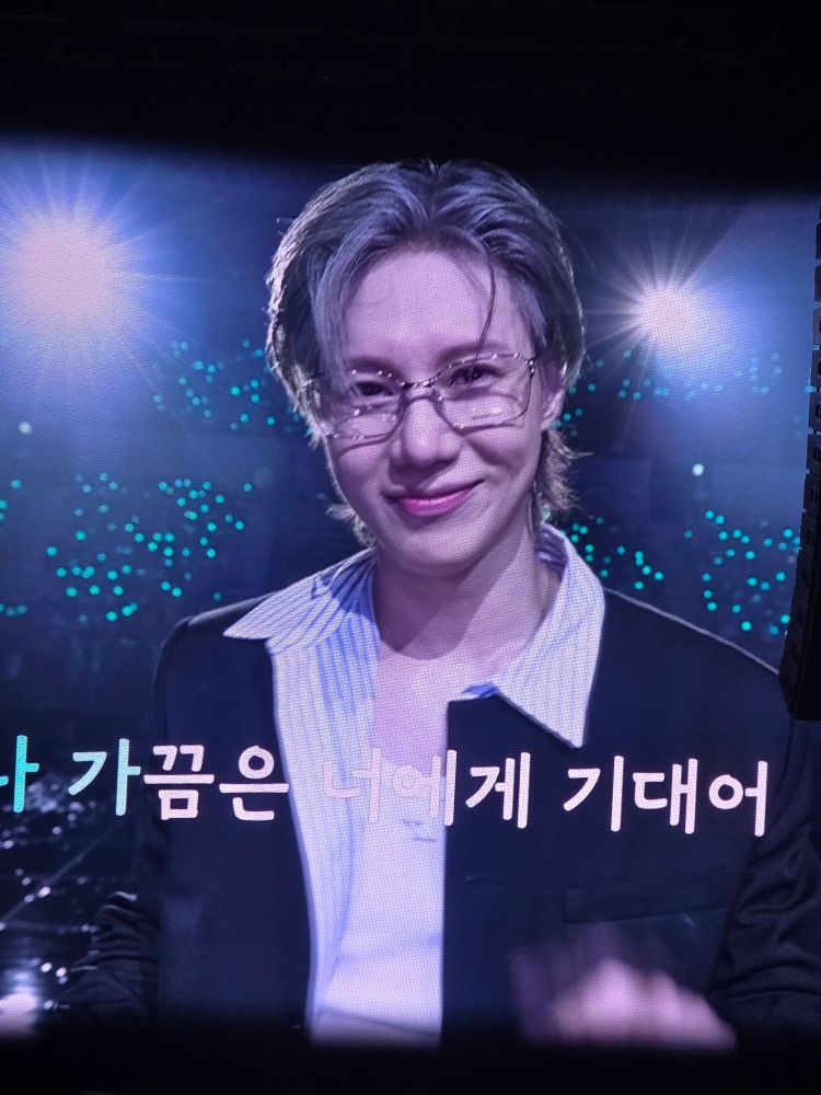Taemin smiling during photo time with his stupid sexy hair showing off his forehead. Credit: @letme_go_home on X.