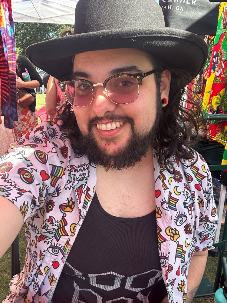 Man wearing a cowboy hat, button up shirt, and tank top that says “Good Boy”