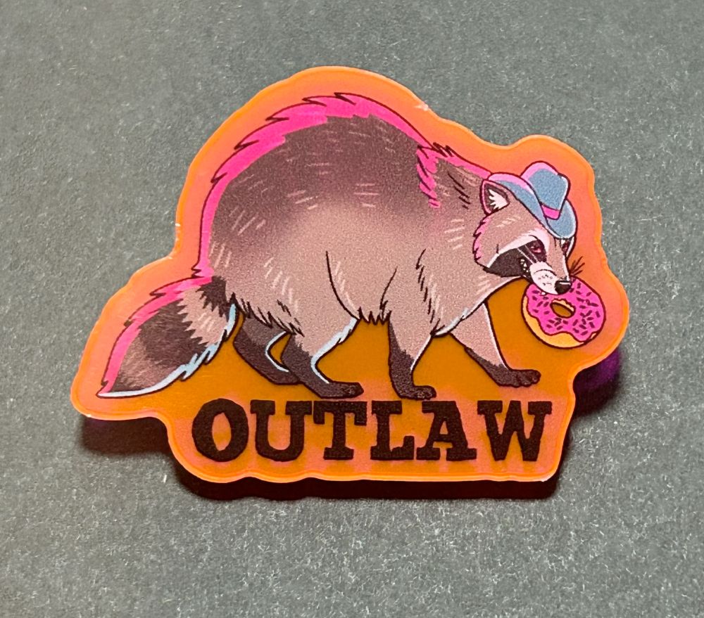 Acrylic pin printed on translucent hot pink/orange acrylic. A raccoon walks to the right, wearing a blue cowboy hat with a pink ribbon. It is holding a pink glazed down and smiling naughtily. It is lit as if by police lights. It says "Outlaw" 