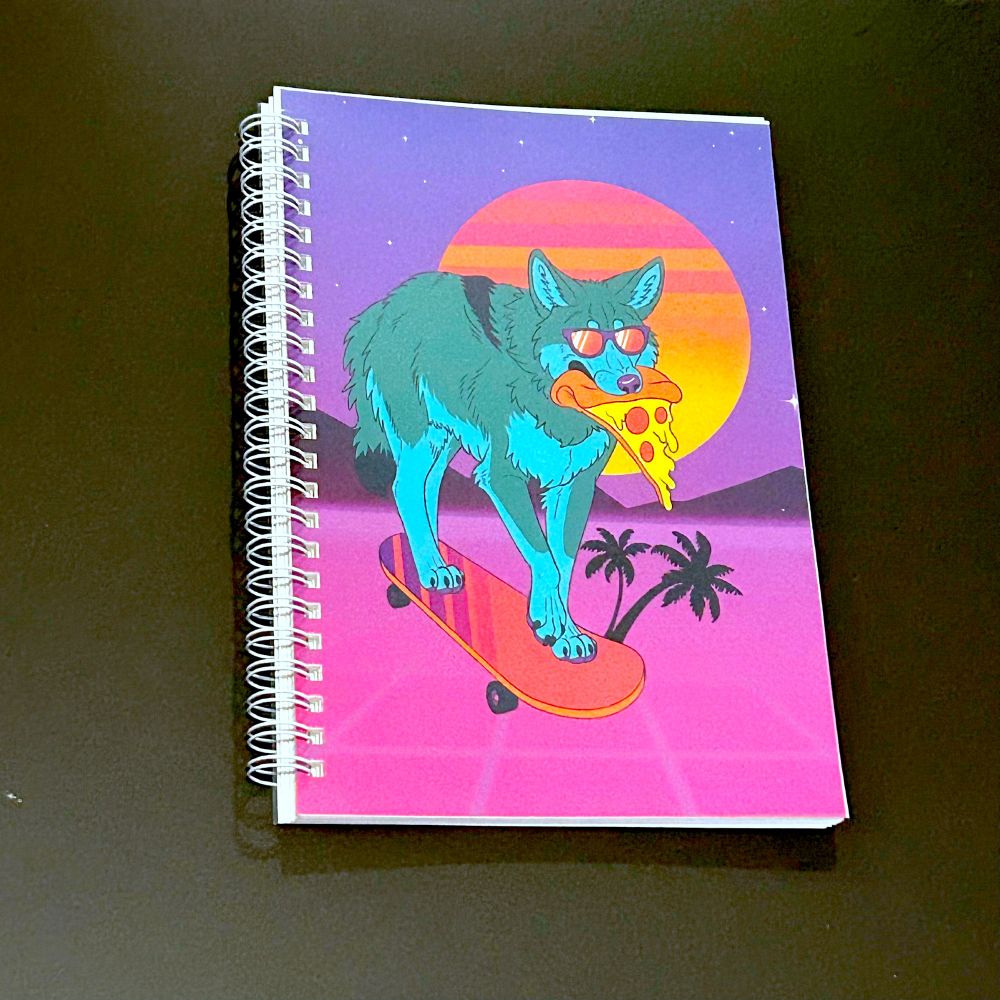 Spiral bound book featuring art of a teal coyote wearing sunglasses and eating pizza as it rides a skateboard away from the sunset 