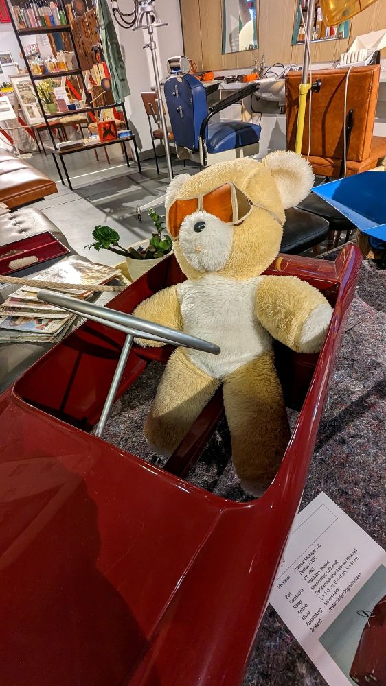 Ein hellbrauner Teddybär mit Sonnenbrille in einem roten Auto