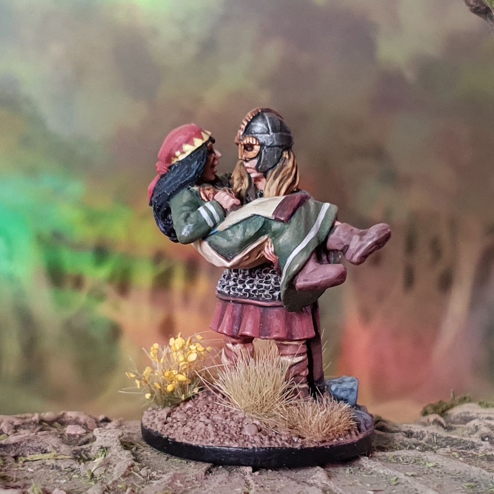 vignette of a shieldmaiden rescuing a female villager. Sculpted by Alan Marsh and shown painted by Here be Goblins. Backdrop of woodland is by Jon Hodgson, with rainbow from a sparkle thingy on it