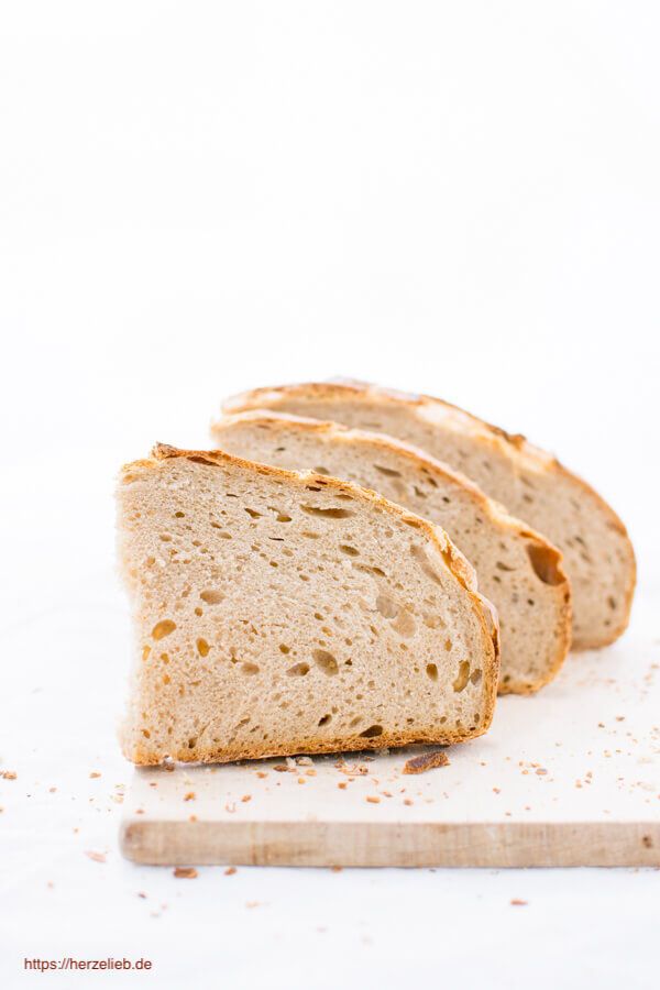 Drei dicke halbe Scheiben von einem saftigen Brot mit einer hellen, lockeren Innenstruktur und einer knusprigen Kruste auf hellem Hintergrund, gebacken nach einem Dinkel-Roggenbrot Rezept von herzelieb.