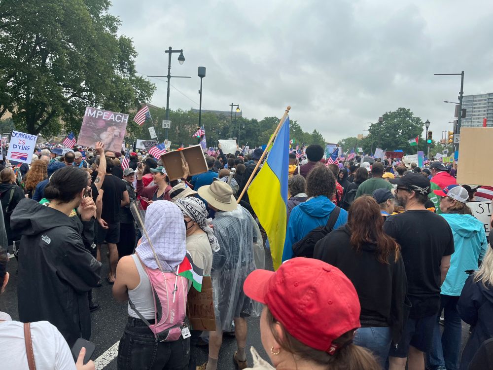 A crowd of protesters in Philadelphia with many signs and flags ranging from the Palestinian flag, the Ukrainian flag, American flags (and upside-down versions). Signs say things like “impeach” and “democracy is dying”. There is no violence or disorder to speak of.