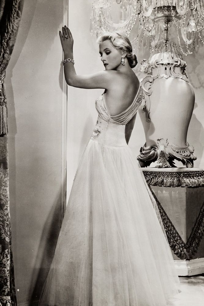 Massie hace de femme fatale un poco a su pesar (aunque su proceso mental y motivaciones no sean el centro de la historia). En esta imagen promocional aparece de cuerpo entero, casi de espaldas con el rostro (con gesto serio) girado de perfil, casi tres cuartos, hacia la cámara, su brazo derecho está apoyada en la pared, en un ambiente lujoso. lleva un vestido claro con falda vaporosa y amplio escote en la espada, que nos permite ver también su costado. Lleva el pelo rubio pulcramente peinado en un moño ajo. 