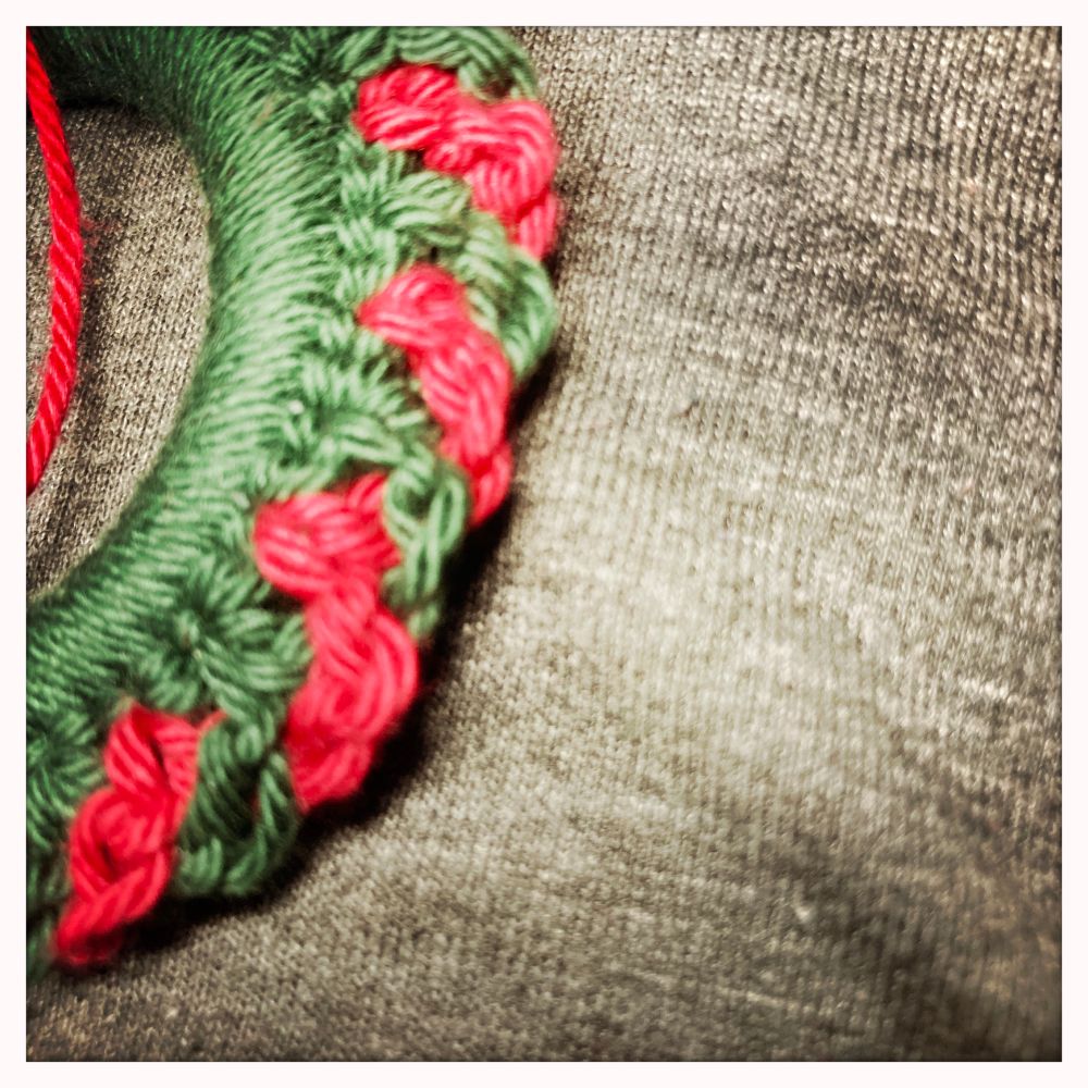 Klein stukje van een haakwerkjevin groen en rood tegen een grijze achtergrond. 
