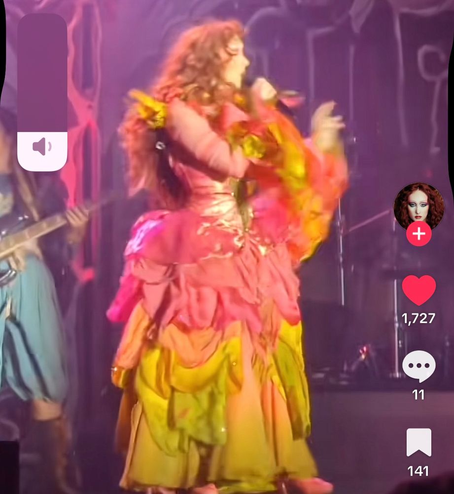 chappell roan performing on stage wearing a pink/orange gown with flowers and ruffles 