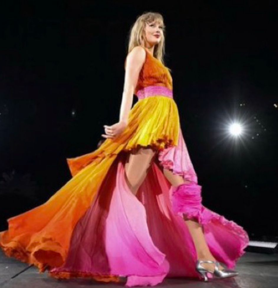taylor swift performing on stage wearing a pink and orange flowy gown 
