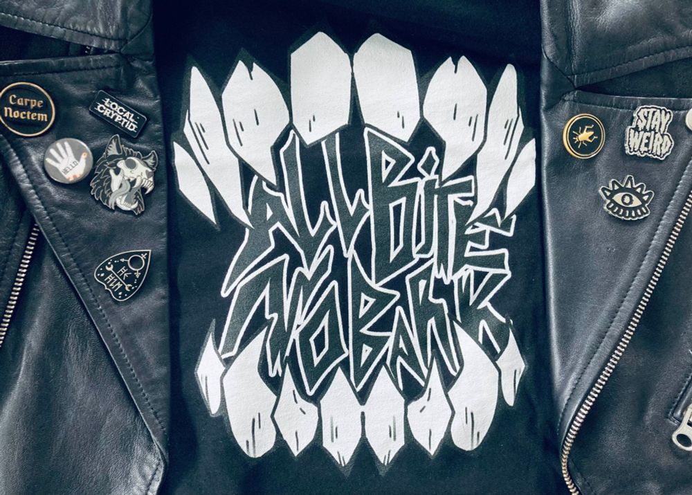 A graphic tank top under a leather jacket with pins. The tank top has a sharp teeth with the words 'All Bite No Bark' inside the mouth.