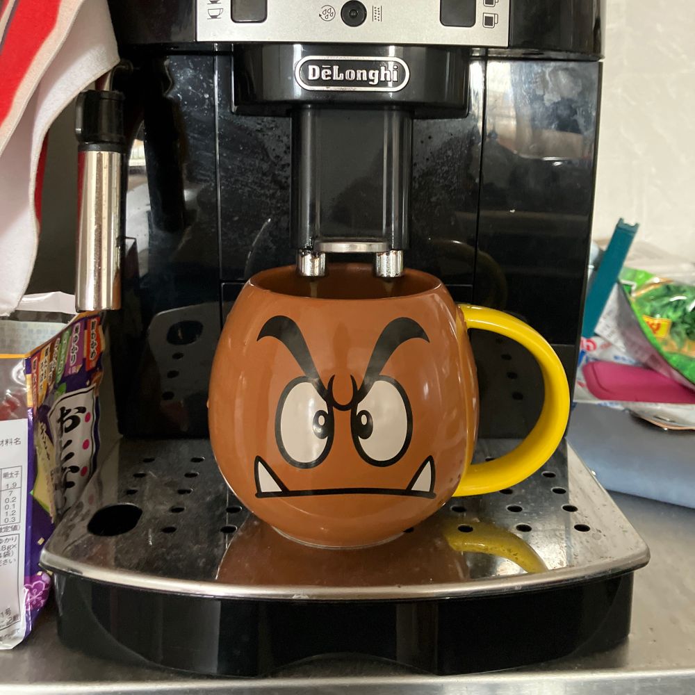 A large brown mug with a cranky face, shaped like a goomba. It is being filled with coffee. 