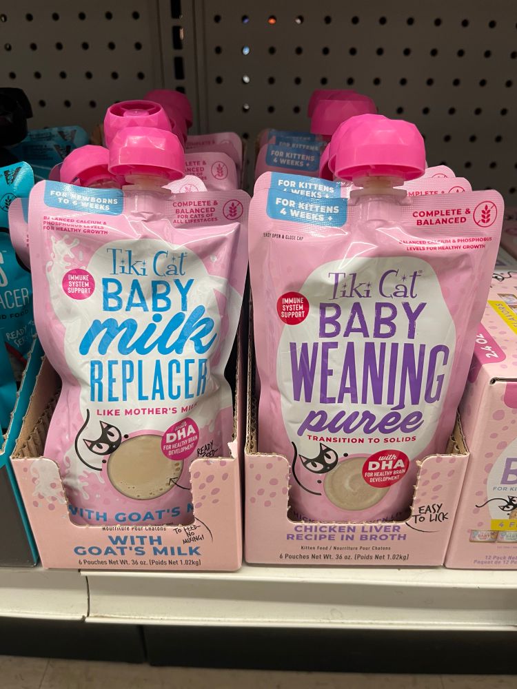 Two pink Tiki Cat brand pouches— one labeled Baby Cat Milk Replacer and the other Weaning Puree.