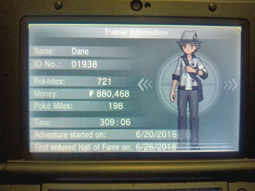 Picture of my Trainer card from Pokemon X showing my trainer wearing a grey feathered hat a black and grey shirt with the sleeves rolled up, black pants and a black over the shoulder bag 
