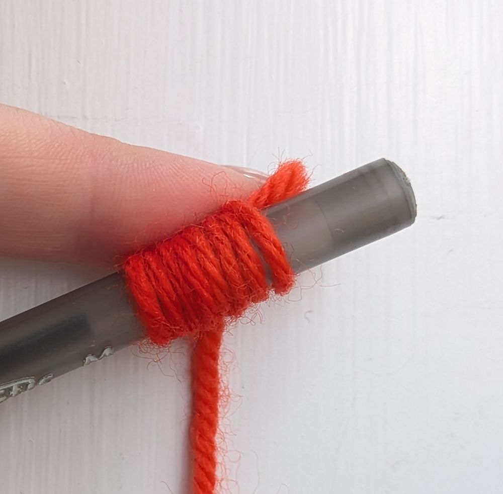 orange yarn wrapped around a grey pen against a white background. Half of the yarn is slightly different than the other half... or is it?