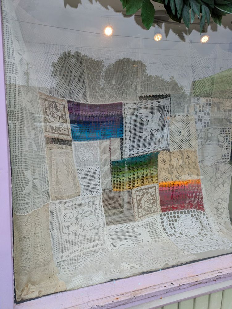 A variety of crochet panels stitched together to form a larger collage. Most of the panels are white/ivory/cream, but three are in color. The colorful panels read LOVERS CANNOT LOSE and are in a variegated rainbow.