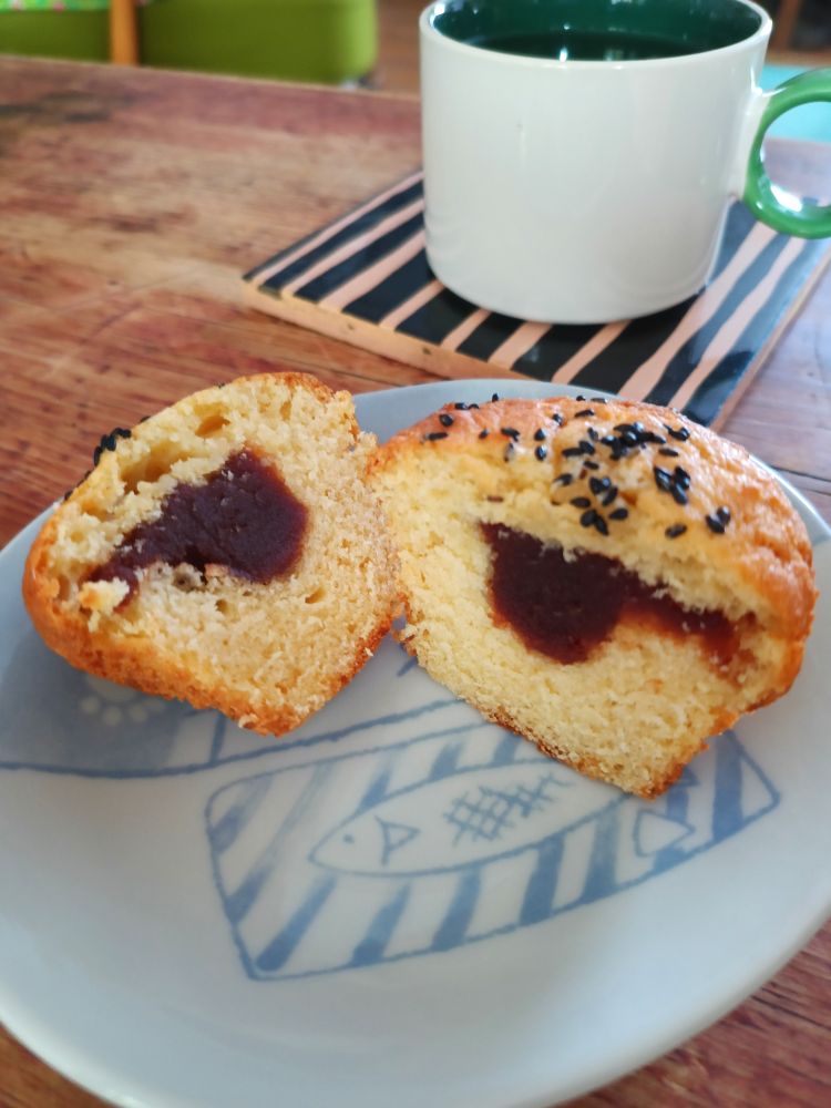 This picture was taken a little later, once muffins had cooled down. It is a photograph of one of the muffins on a plate next to a cup of buckwheat tea (I wanted to continue the Japanese theme). I have chopped the muffin in half so you're looking at two cross-sections. You can see the red bean paste sitting inside the muffin is sitting on a plate that has a picture of a fish on it. 