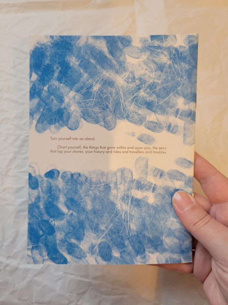back cover of the same zine, covered in monoprint thumbprints and held by a hand to show scale. blurb reads: Turn yourself into an island. chart yourself, the thingst hat grow within and upon you, the seas that lap your shores, your history and tides and travellers and troubles.