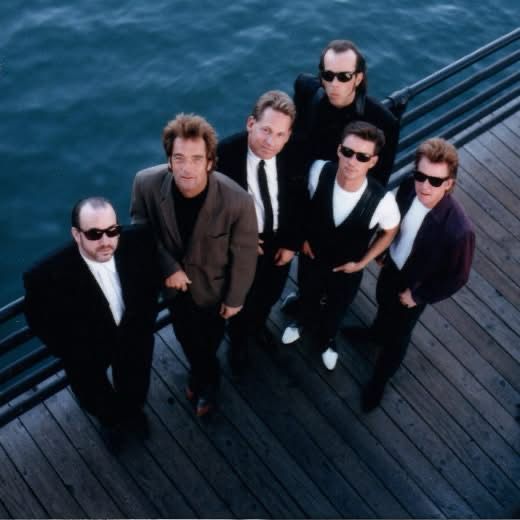 Huey Lewis and the News on a dock by the ocean all looking upward 
