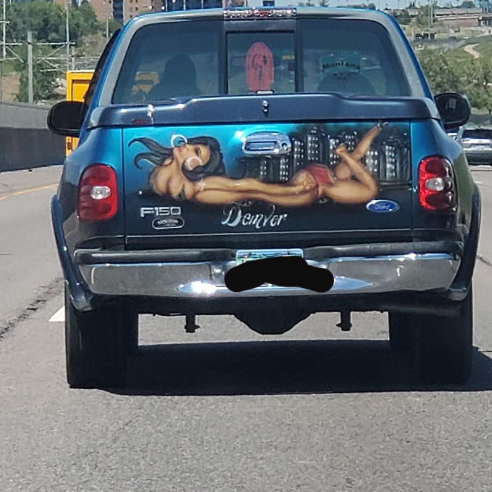Art on the back door of a Ford F-150 truck of a woman with very poor anatomy proportions, where her torso and arms is ridiculously long, her breasts are orbs up on her neck, and the word "Denver" is superimposed on it