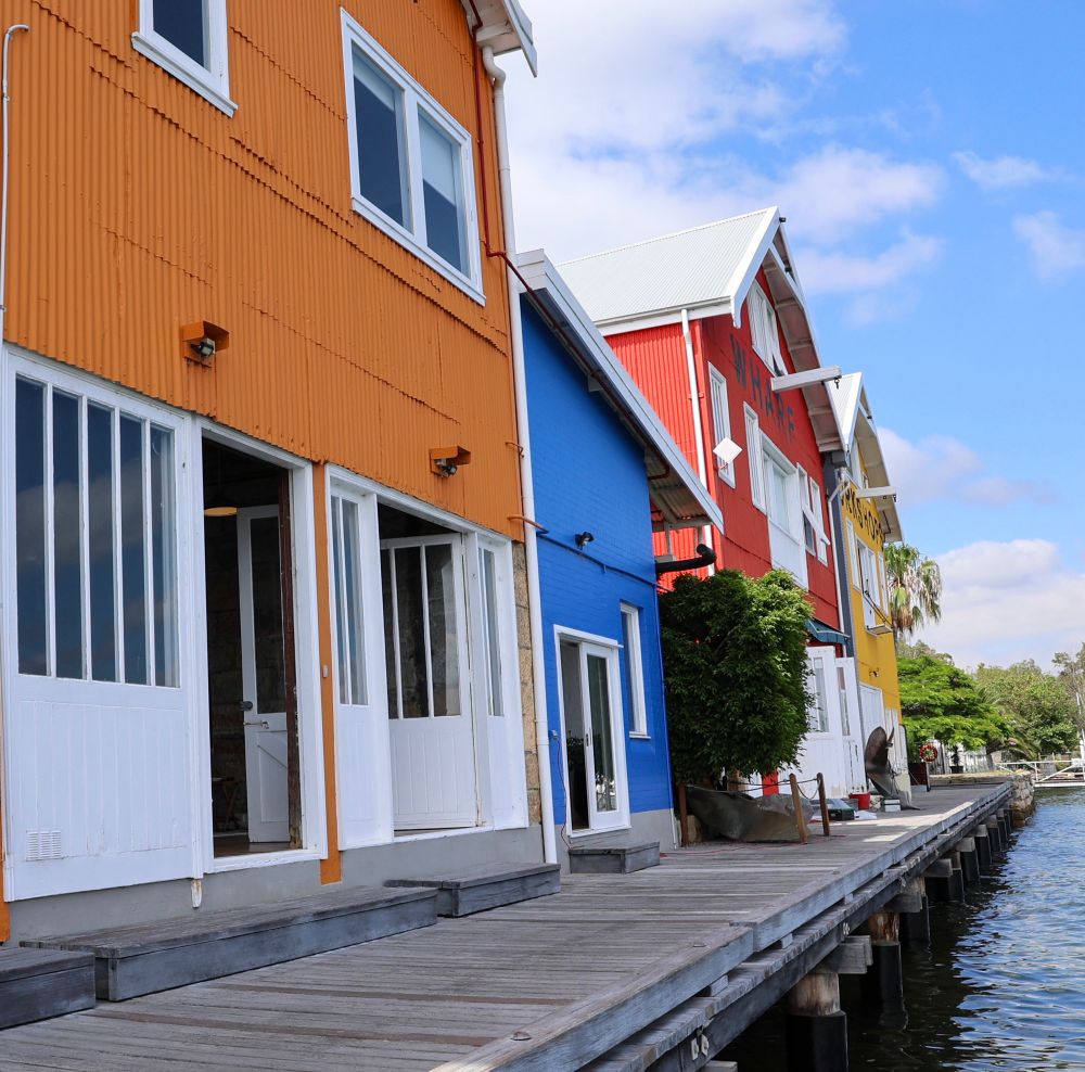 Photo of colourful houses (orange, blue, red, and yellow) on a wharf in front of the water