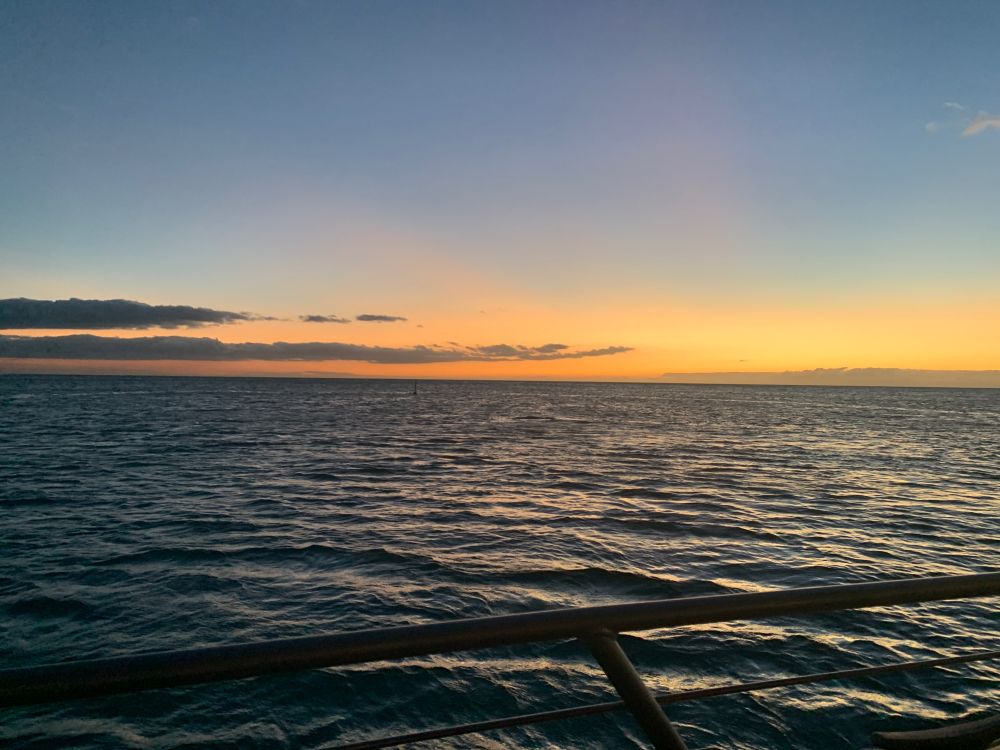Orange and red sunset over the Pacific Ocean in Hawaii.  Wispy clouds drifting over on left side of picture. Wave ripples on the water.