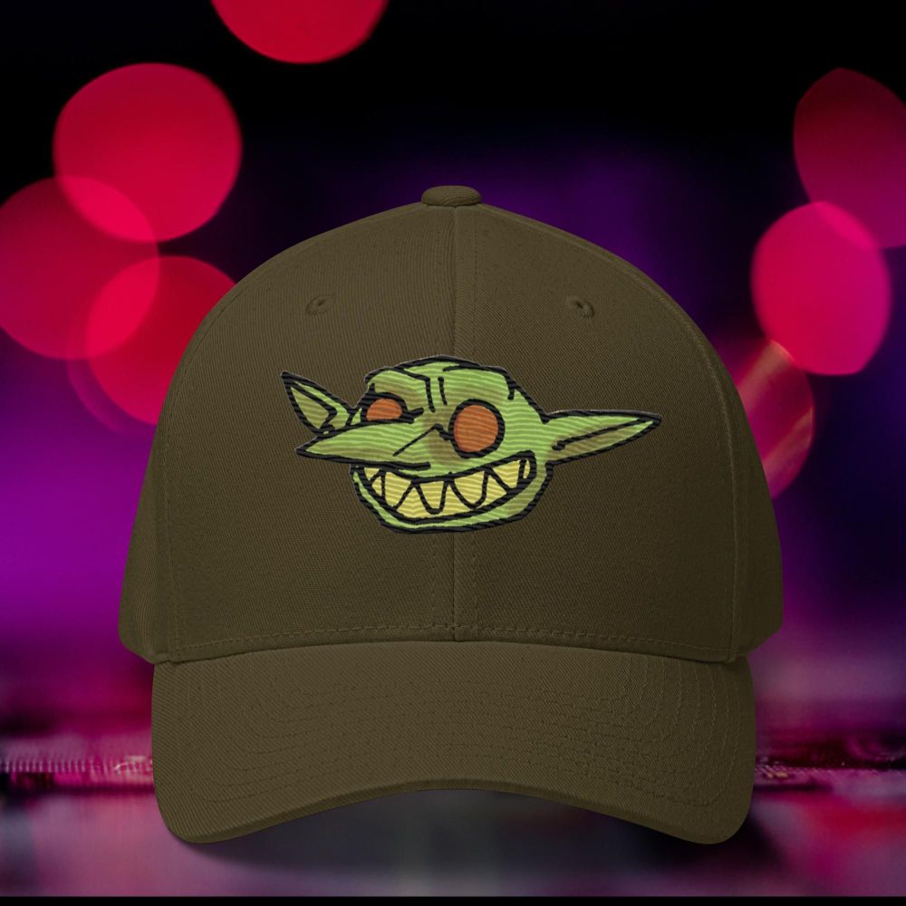 An olive baseball cap with a mischievous goblin from Vast embroidered on it.