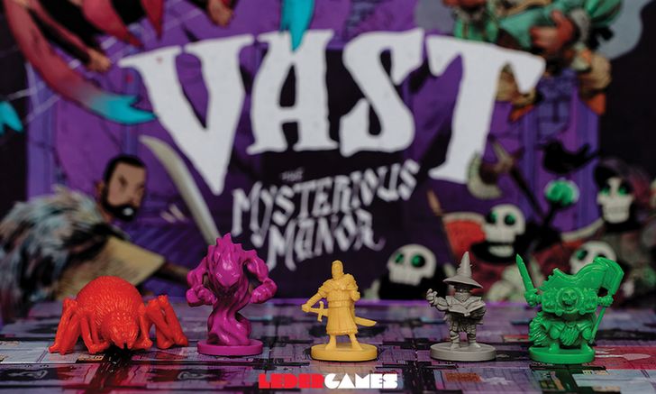 Vast: The Mysterious Manor game box, blurred in the background. In the foreground, the main characters' minis sitting on the game tiles. A giant spider, a phantom, a paladin, a warlock, and a skeleton.
