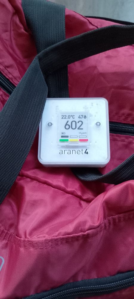 A red soft bag with an aranet 4 sensor on top. 
The sensor shows 22C temperature, 47% humidity, and a CO2 level of 602.