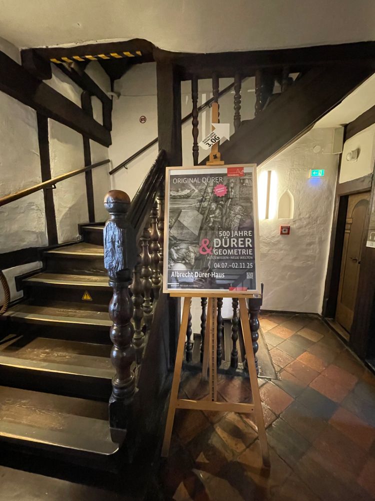 A staircase in Albrecht Dürer's house with a poster next to it for the "500 years Dürer and Geometry" celebration. 