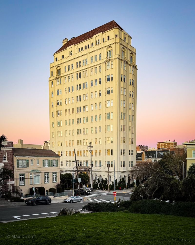 A tall apartment building on a small lot that is surrounded by single family homes.