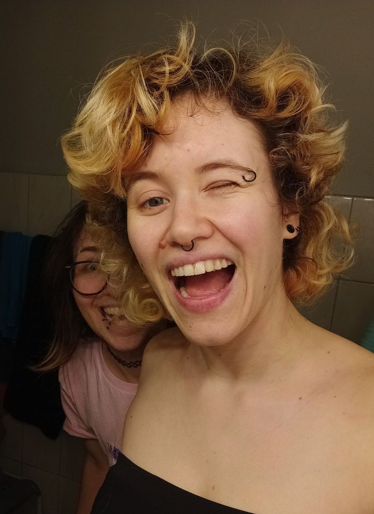 me and alex laughing excitedly in a bathroom. my hair is bleached, curly and about chin length