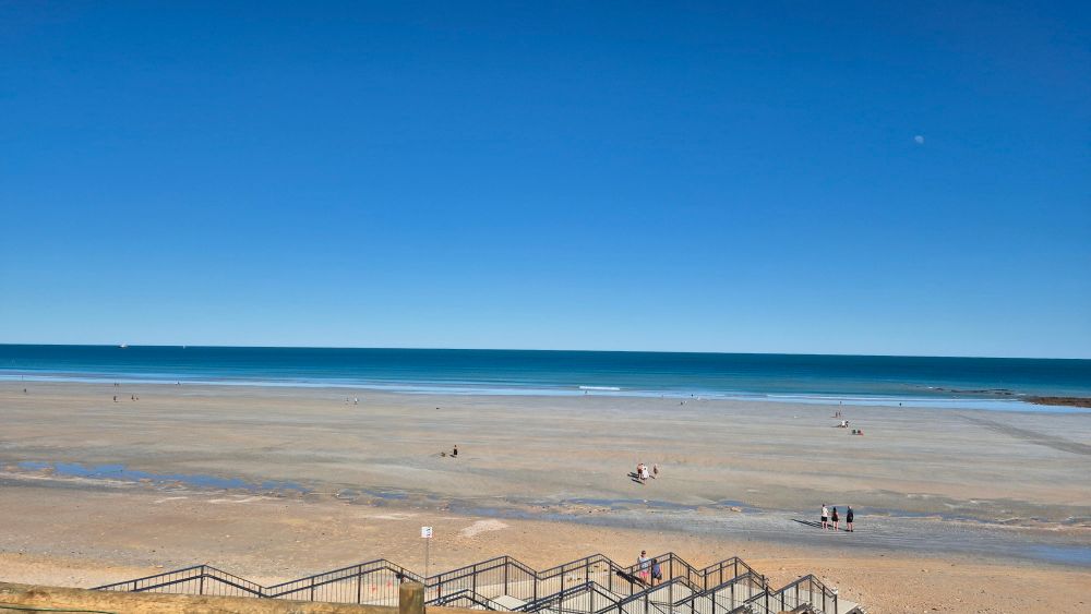 Cable beach low tide. Stairs leading down to wide beach with water in distance. Blue sky. 