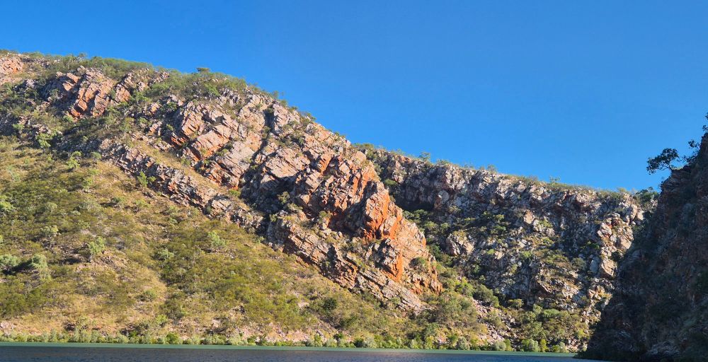 Rocky crop with rusty iron colouring, green spinifex and blue sky. 