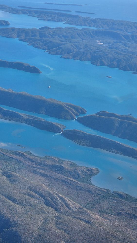 A view from the air of the horizontal falls, where you can see white water at the narrowest point of both gaps. Blue water, faded green hills. 