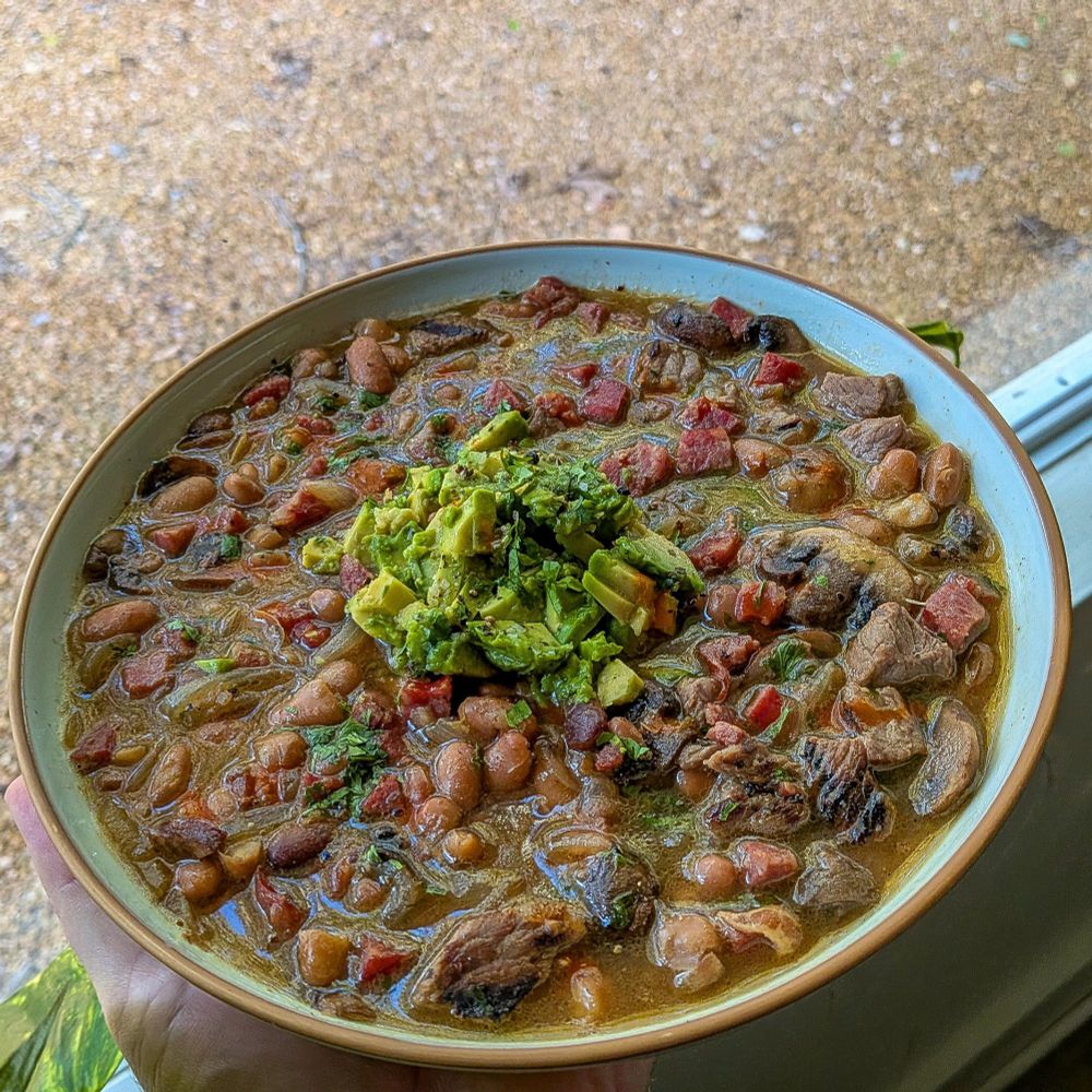 A bowl of pinto beans with leftover steak, mushrooms, habanero sausage, topped with fresh avocado. 