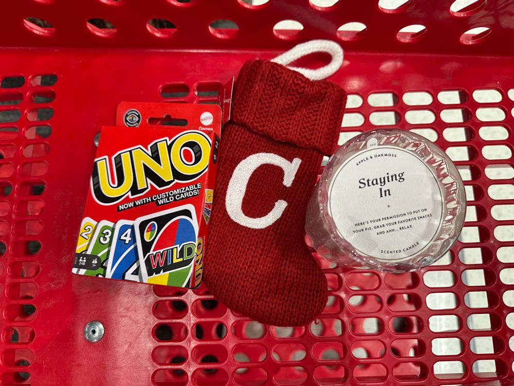 A picture of an Uno set of cards, a small stocking with a “C” on it, and a candle that says “Staying In.”