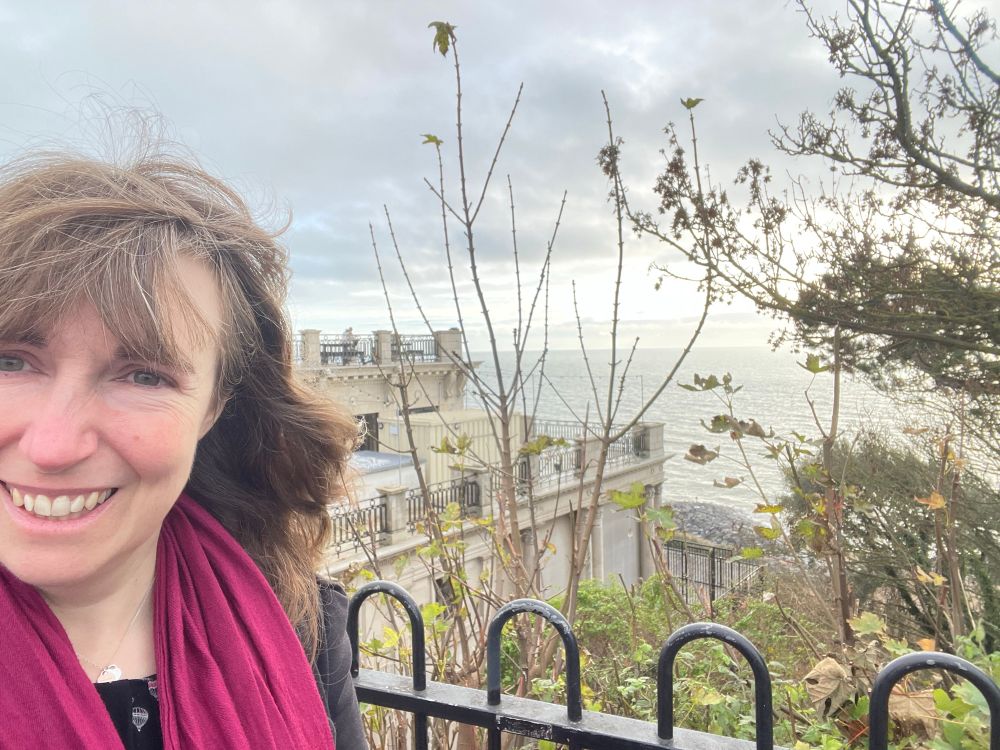 A selfie of a smiling woman with a view of the sea in the background.