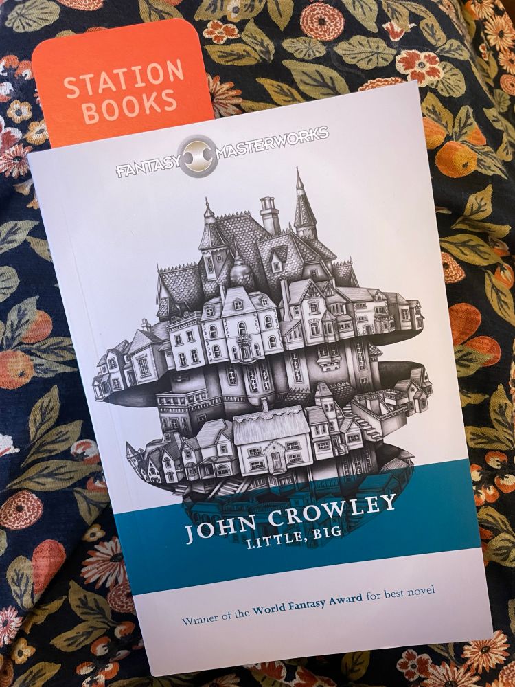 A photograph of a book: Little, big by John Crowley. A bookmark for Station Books pokes out of the top. The cover is white with a black line drawing of lots of buildings, most likely houses, laid out as if they are in some kind of spinning top. Underneath is the text: Winner of the World Fantasy Award for best novel.