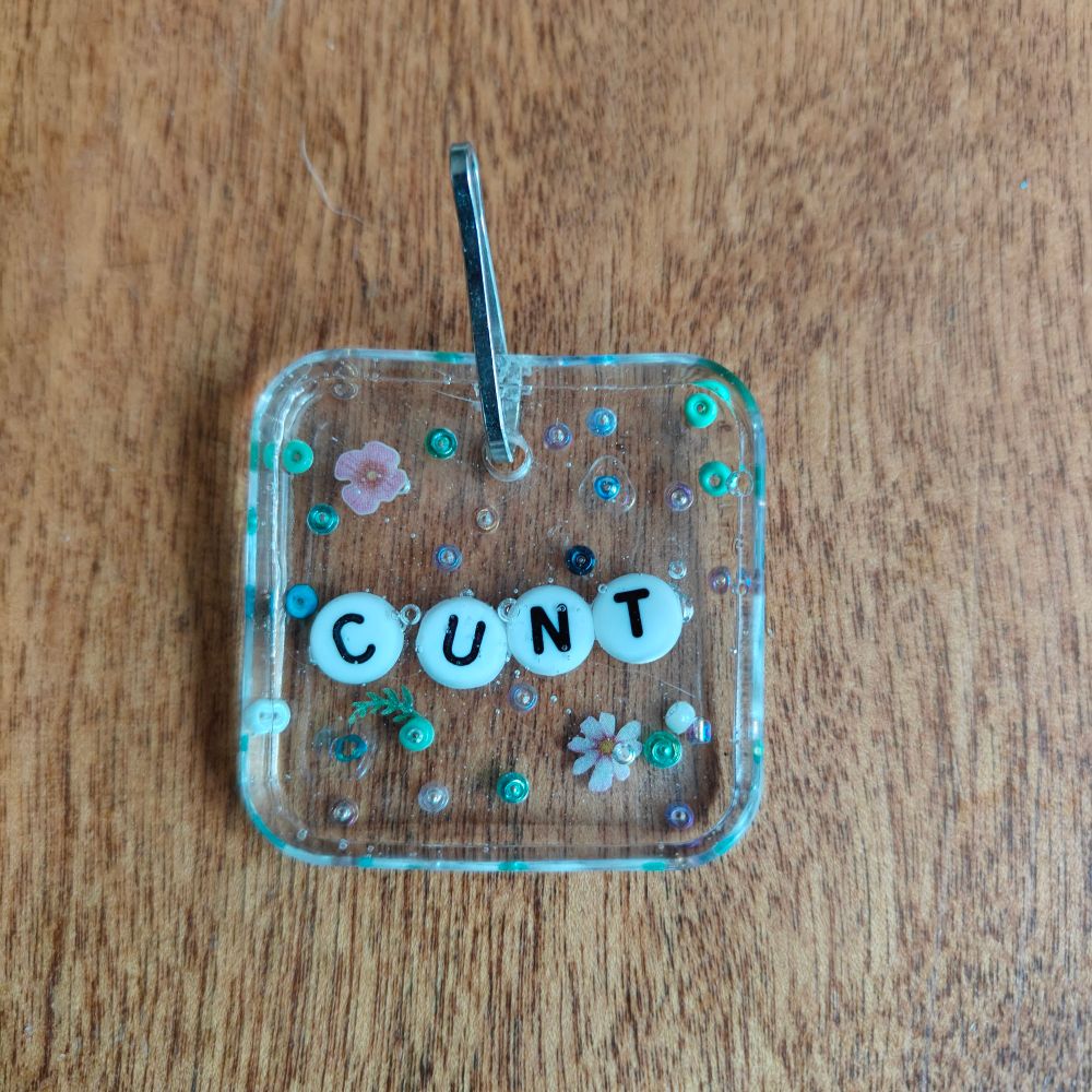 Feminine, demure little resin pendant, with flowers and beads, that says cunt
