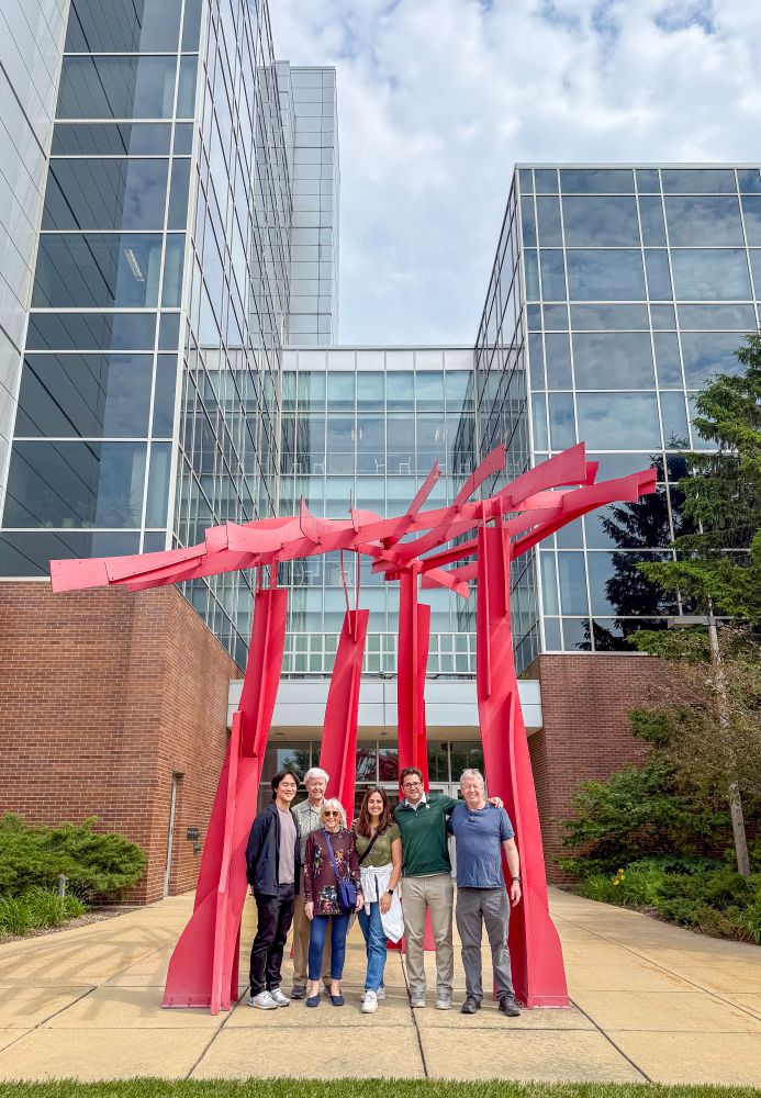 Terry Dardas & his family are joined by MGI doctoral student Tom Kim. They are standing in front of the red sculpture in front of BPS. 
