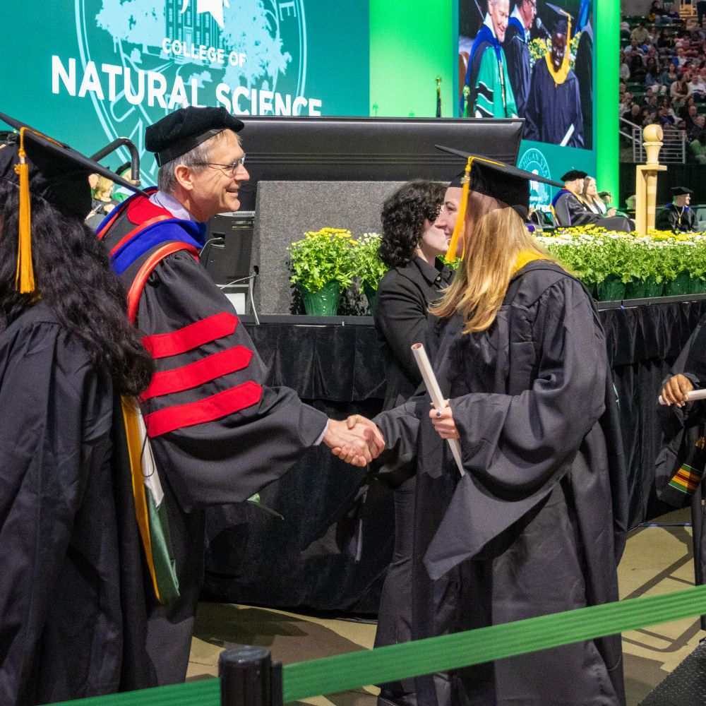 A masters graduate shakes hands with Dean Eric Hegg as she receives her diploma. 
