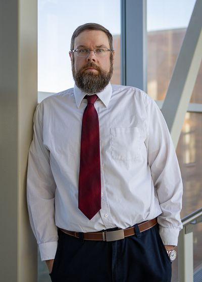 Phillip C. Delekta looks at the camera. He is wearing a white shirt and red tie and is standing in front of a window. 
