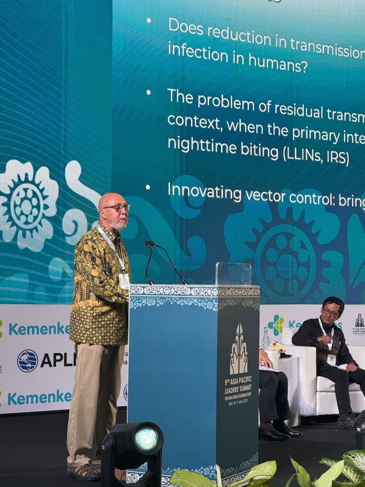 Ned Walker gives the keynote address. He's standing behind a lecturn, and there is a large screen behind him. He's wearing a colorful patterned shirt, khaki pants, and sandals. 
